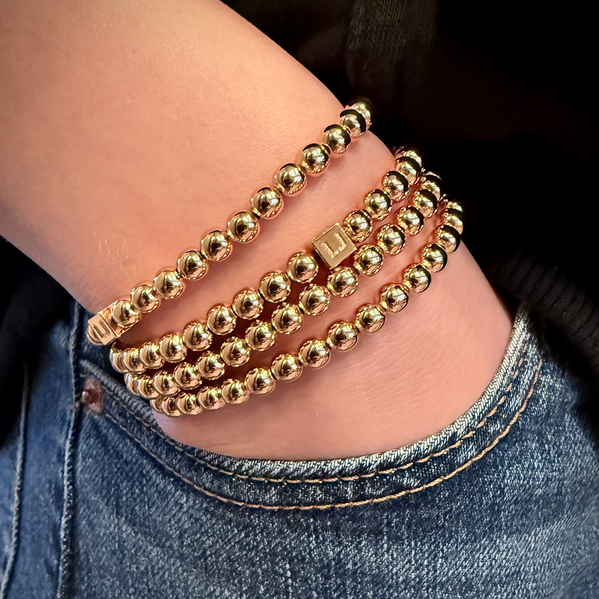 Gold beaded bracelets on a wrist with a denim background