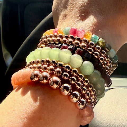 Hand wearing multiple colorful beaded bracelets with a blurred background