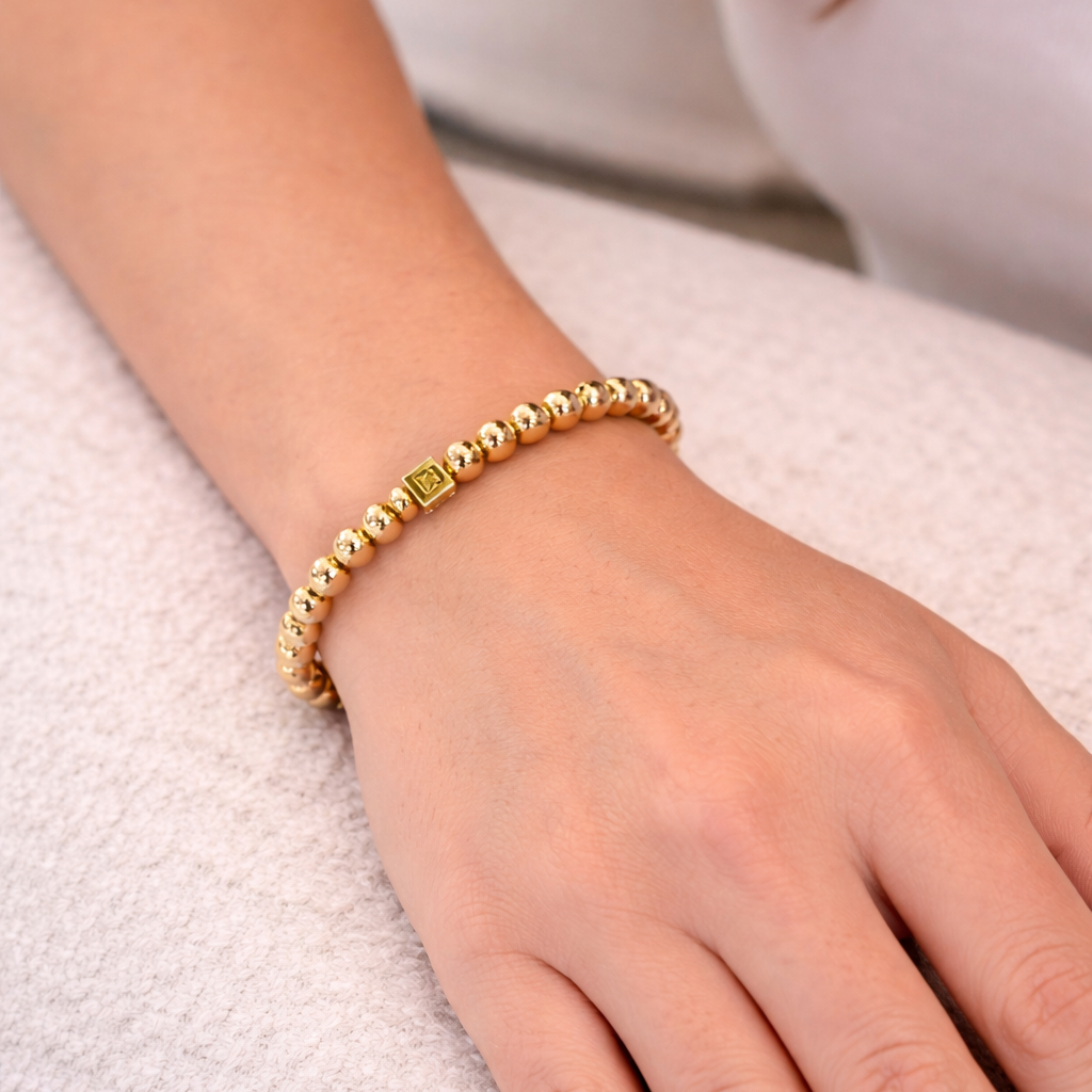 Gold beaded bracelet on a person's wrist against a white background