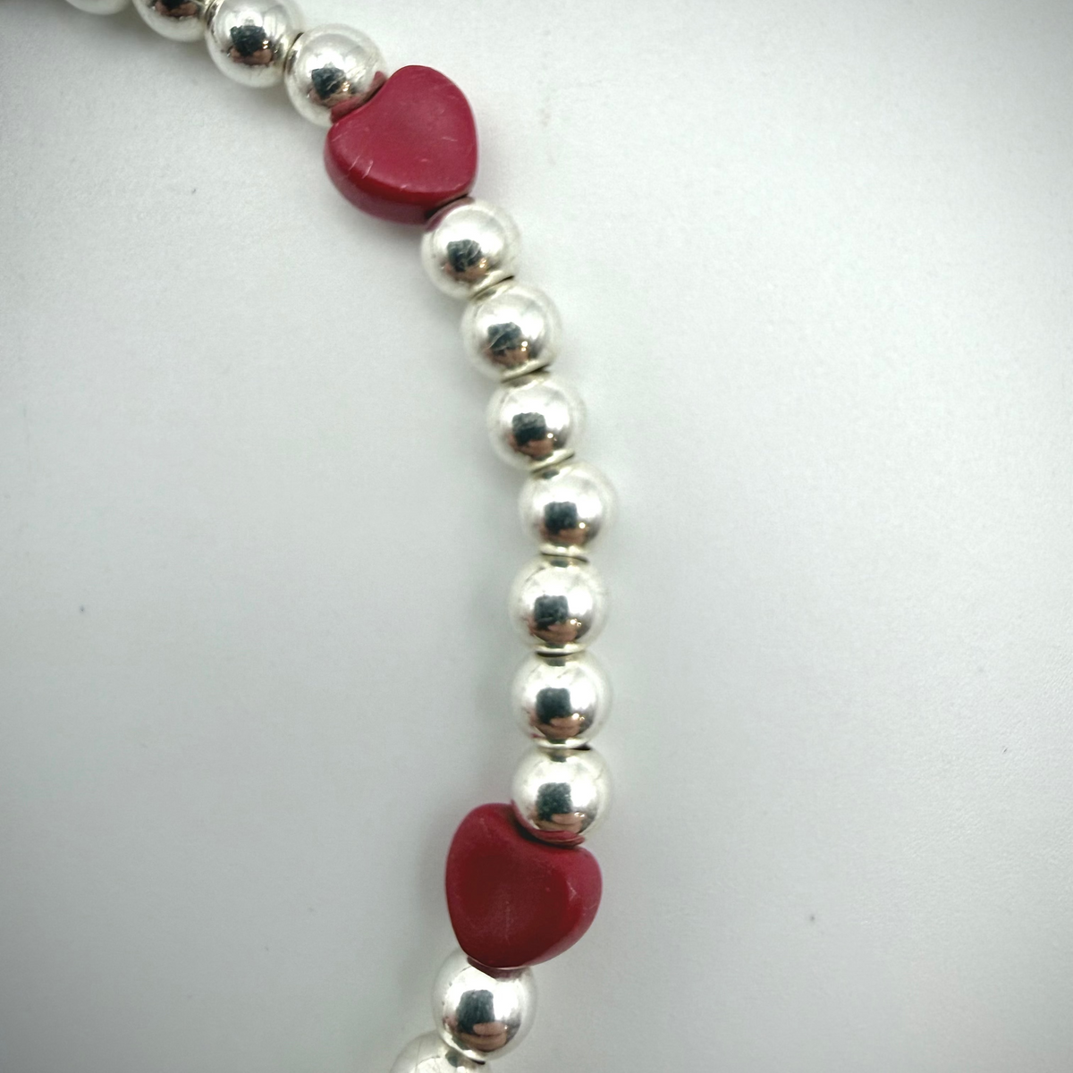 Silver beaded bracelet with red heart-shaped charms on a white background