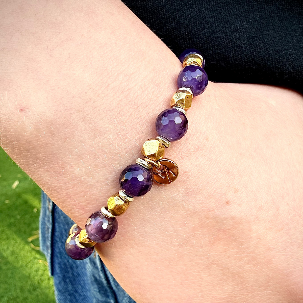 Bracelet with purple and gold beads on a wrist against a grassy background