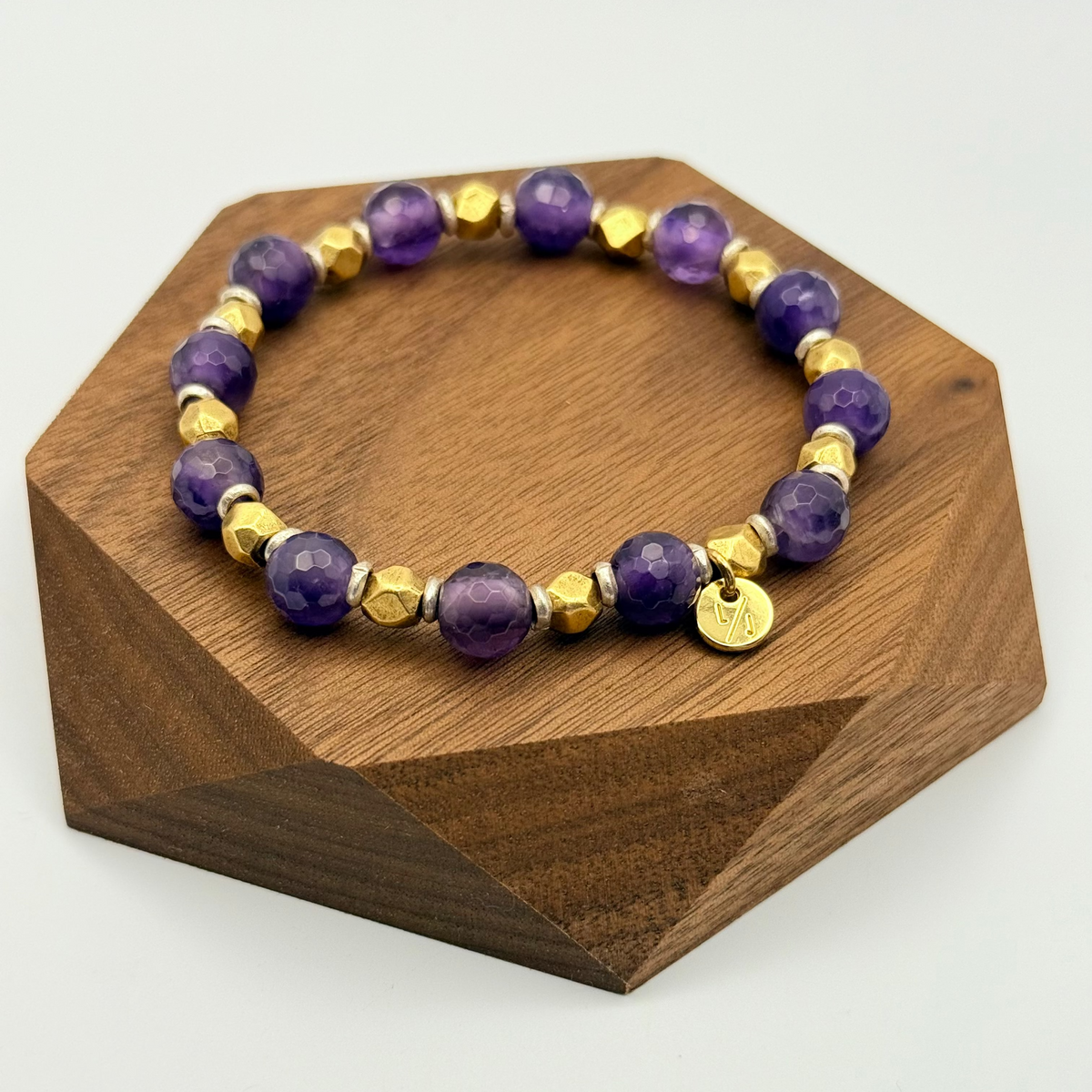Purple beaded bracelet with gold accents on a wooden stand
