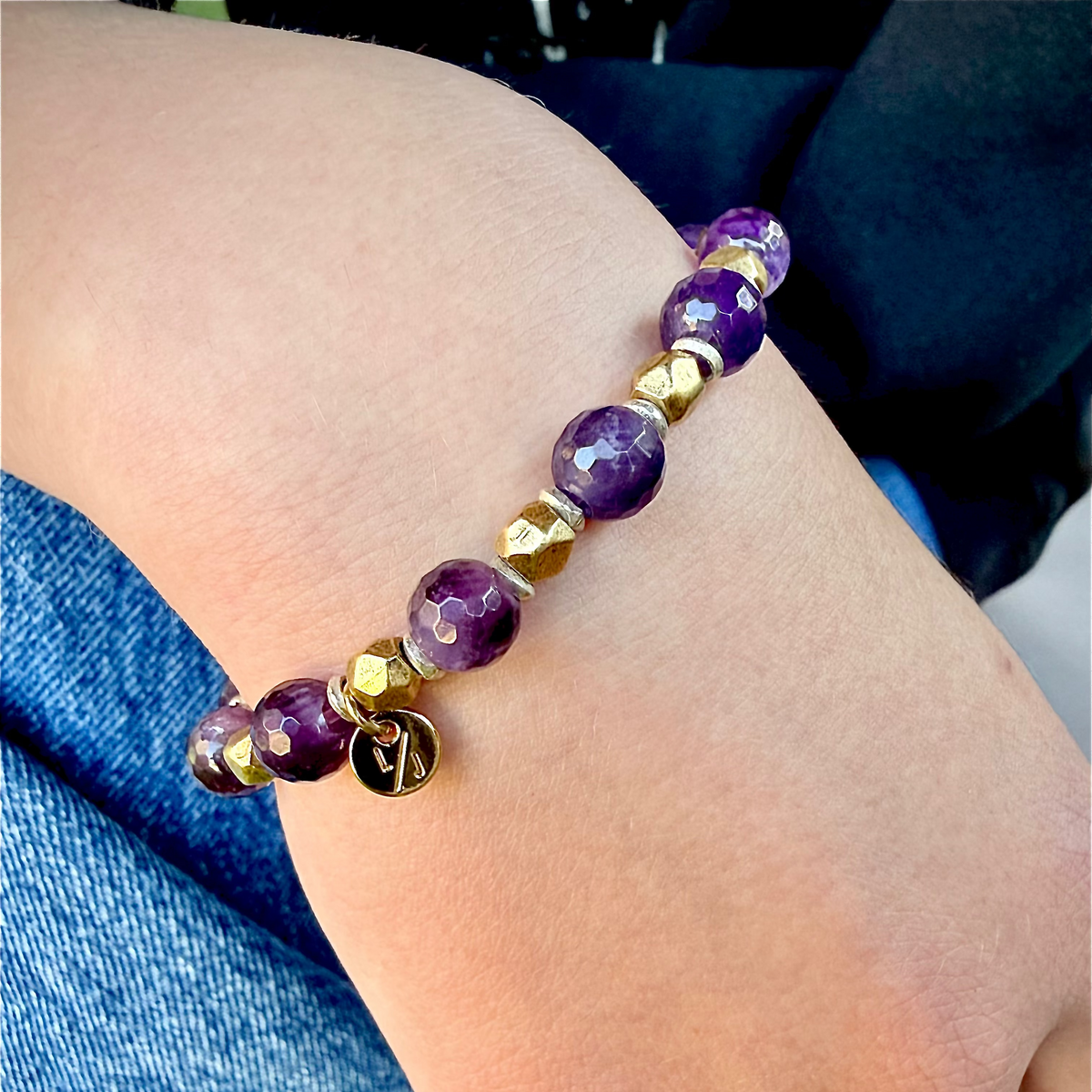 Purple beaded bracelet with gold accents on a wrist against a blue jeans background