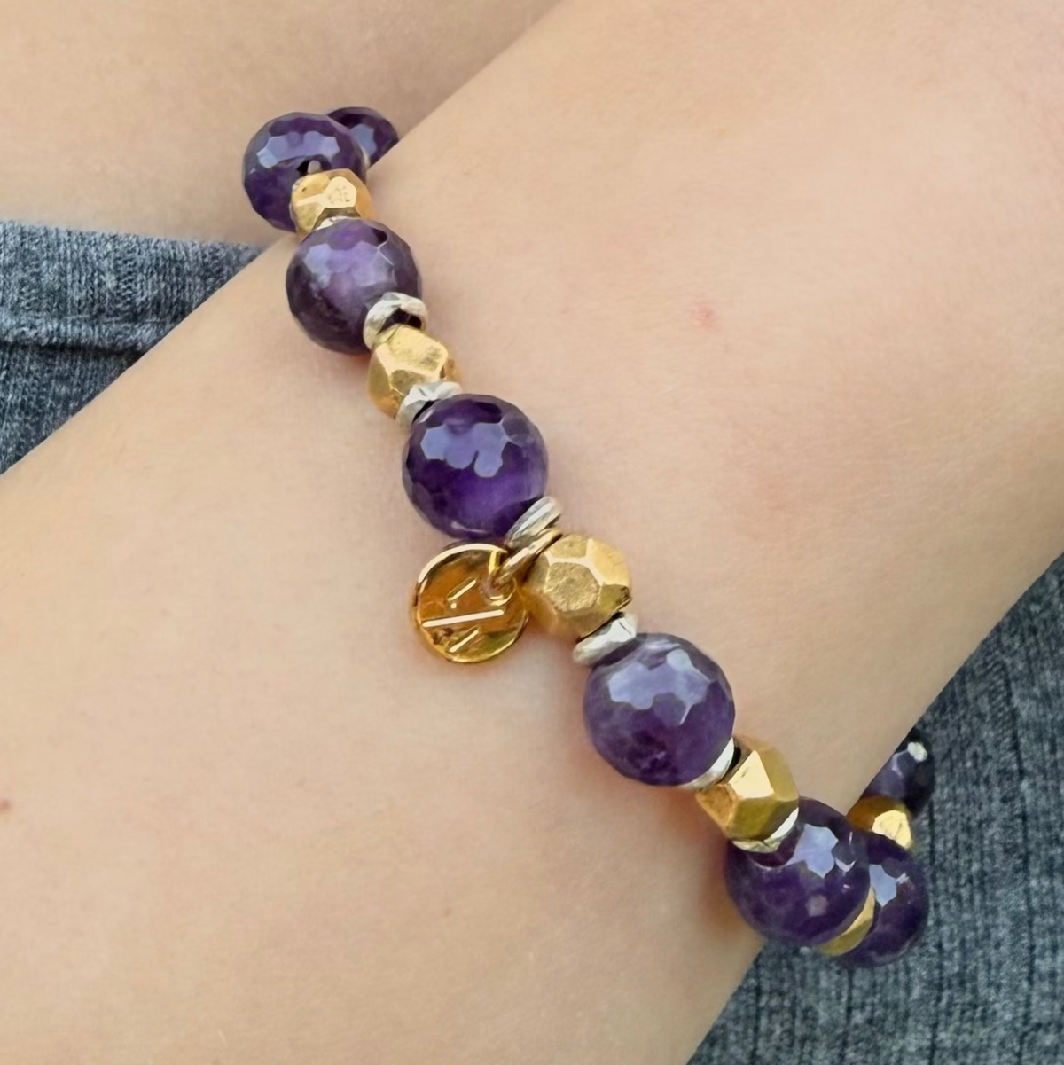 Purple beaded bracelet with gold accents on a wrist against a neutral background
