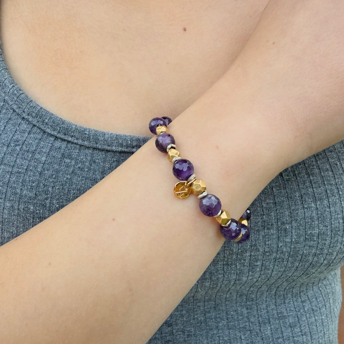 Bracelet with purple and gold beads on a wrist, wearing a gray sleeve.