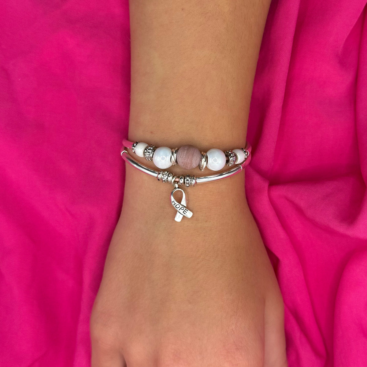 Bracelet with a pink ribbon charm on a wrist against a pink fabric background