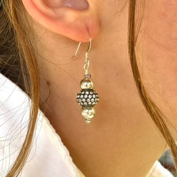 Close-up of a person wearing silver earrings with beads.