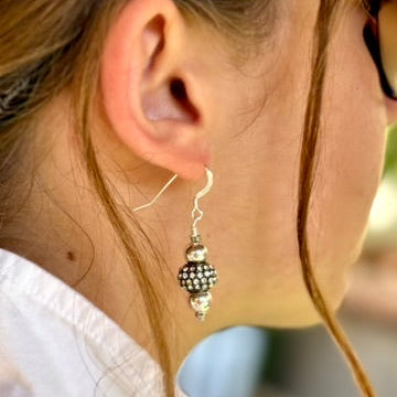 Close-up of a person wearing a silver earring with a bead detail.