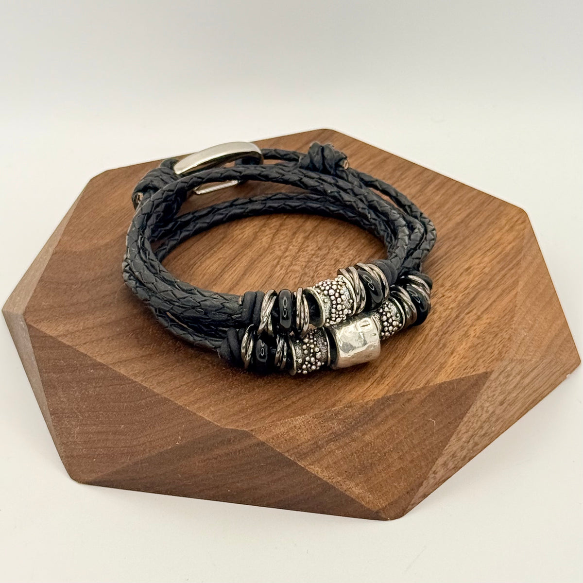 Black braided leather bracelet with metal beads on a wooden stand