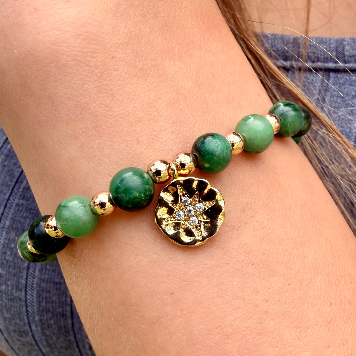 Bracelet with green beads and a gold charm on a wrist against a denim background