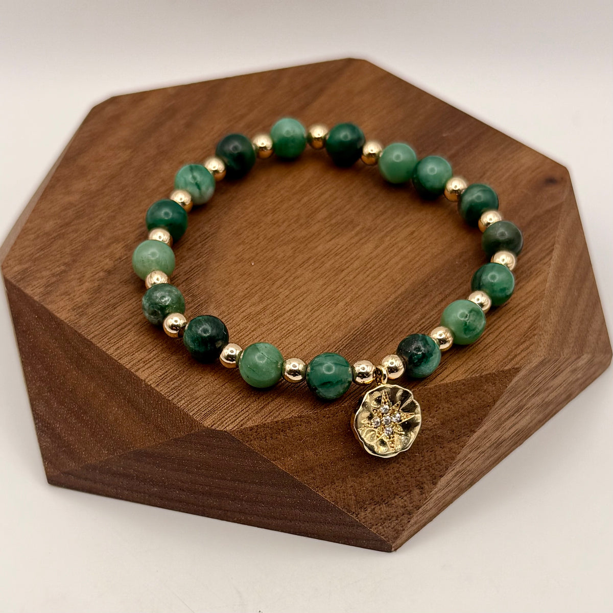 Green beaded bracelet with gold accents on a wooden stand