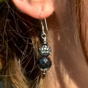 Close-up of an earring with a black bead and silver hook.