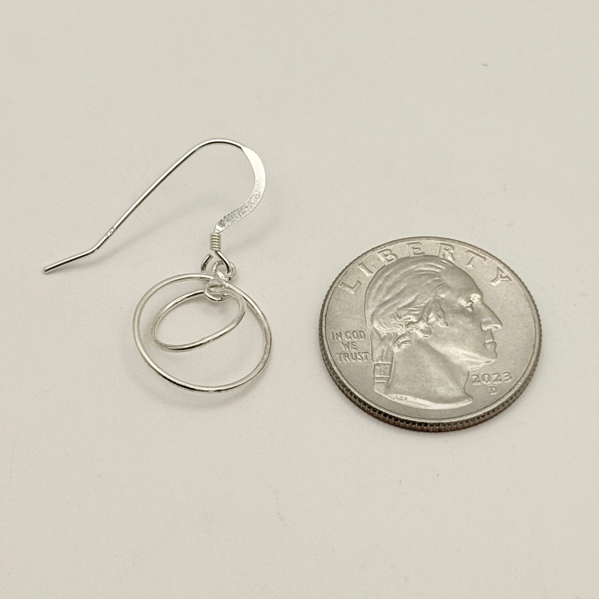 Silver hoop earrings next to a U.S. quarter for size comparison on a light gray background