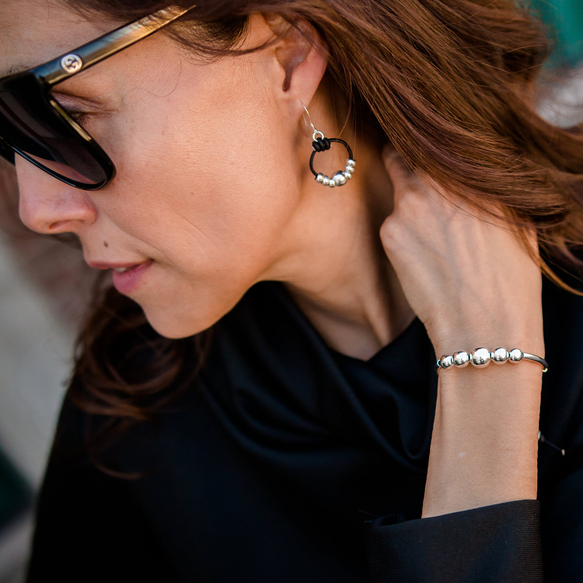 Woman wearing sunglasses, earrings, and a bracelet on a blurred street background