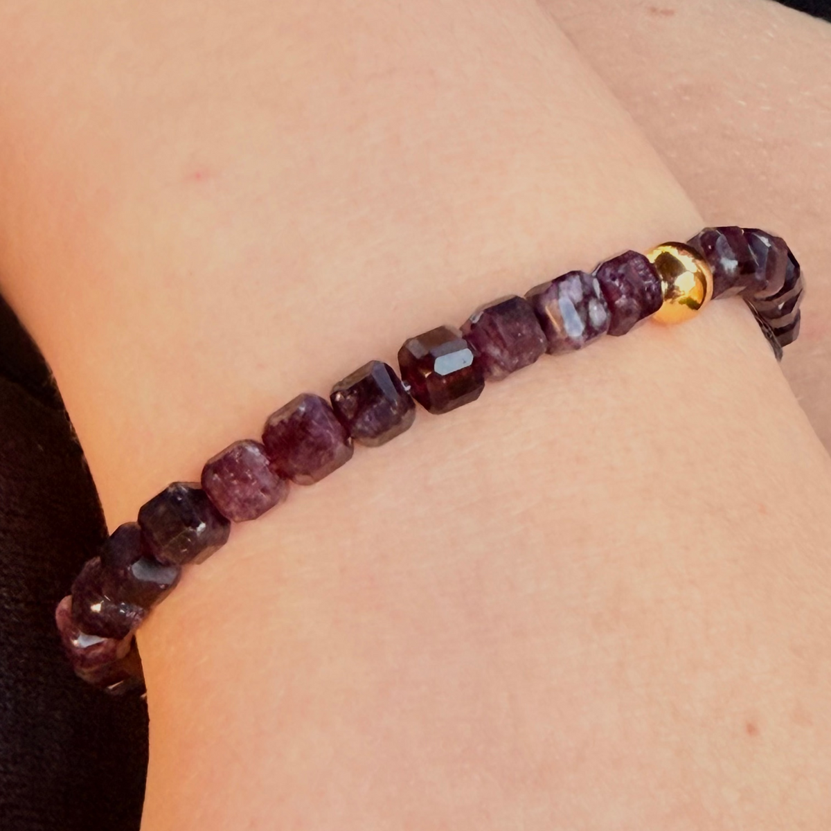 Garnet beaded bracelet with a gold accent on a wrist against a dark fabric background