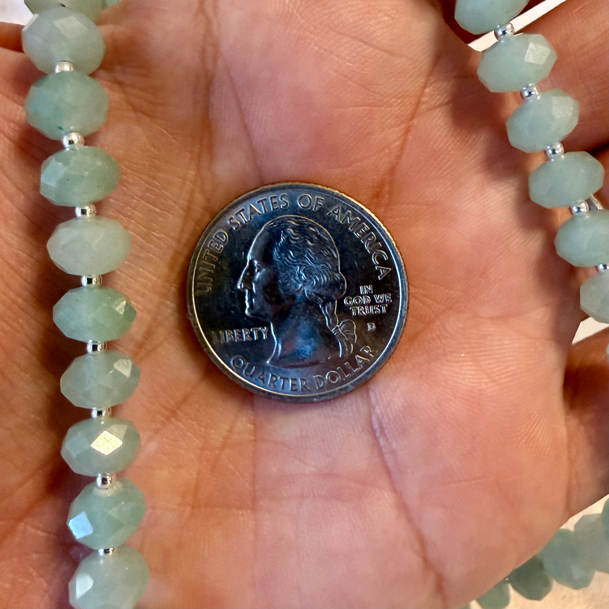 Faceted light green gemstone beads on a necklace draped over a person's hand, with a U.S.