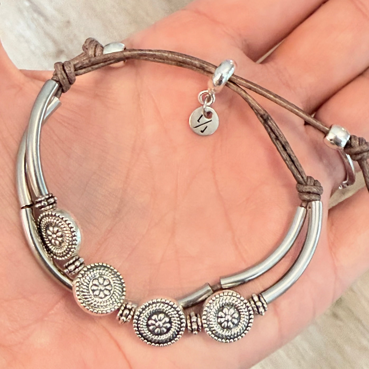 Silver bracelet with decorative elements on a hand against a neutral background