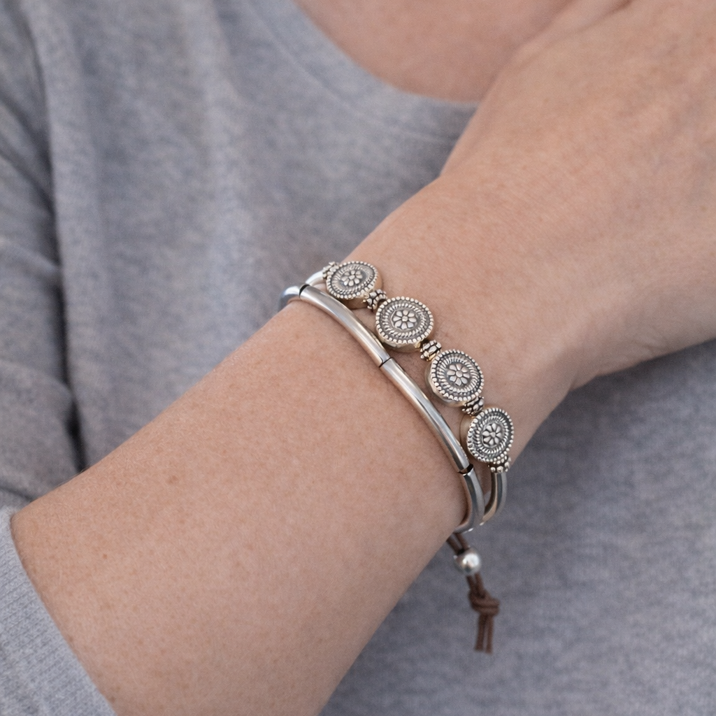 Close-up of a person's wrist wearing a silver bracelet with circular designs on a gray background