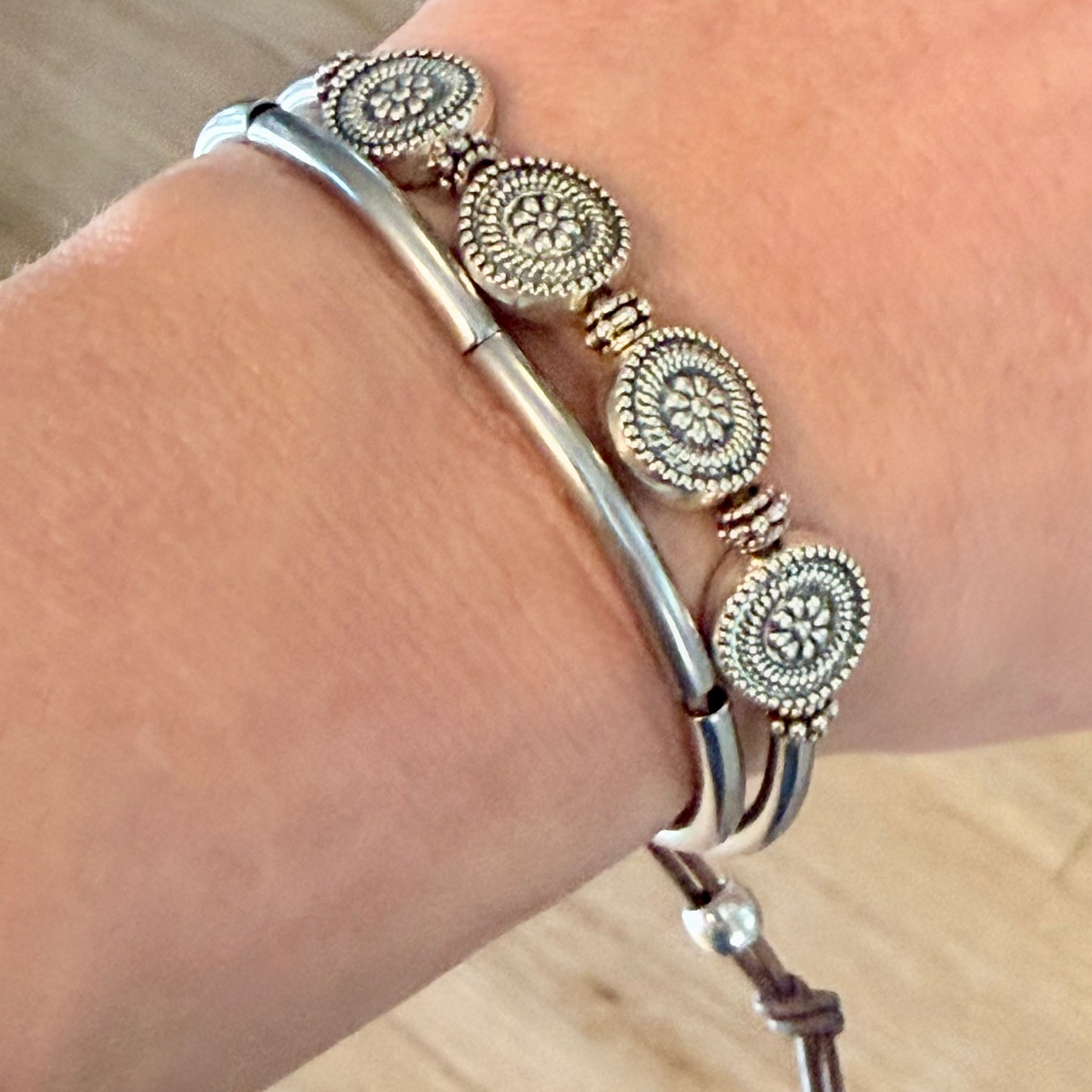 Silver bracelet with circular designs on a wrist against a wooden background