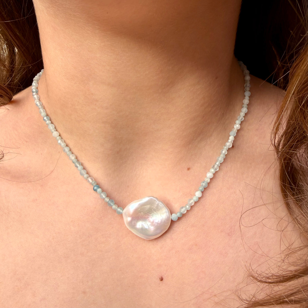Pearl necklace with a large central pearl worn by a person