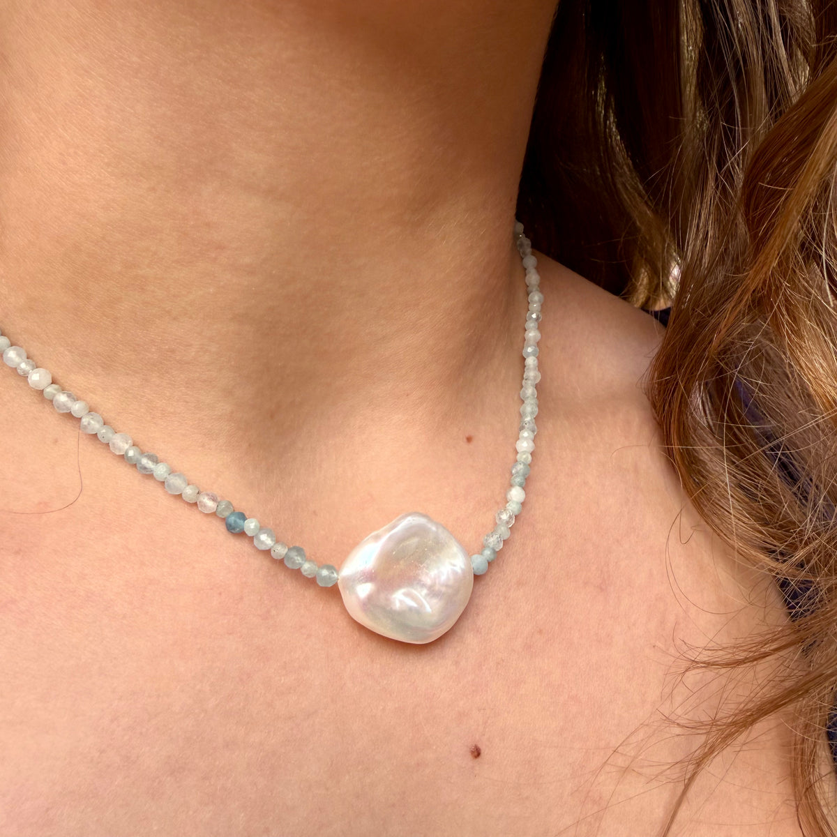Pearl necklace with a large baroque pearl pendant on a person's neck.