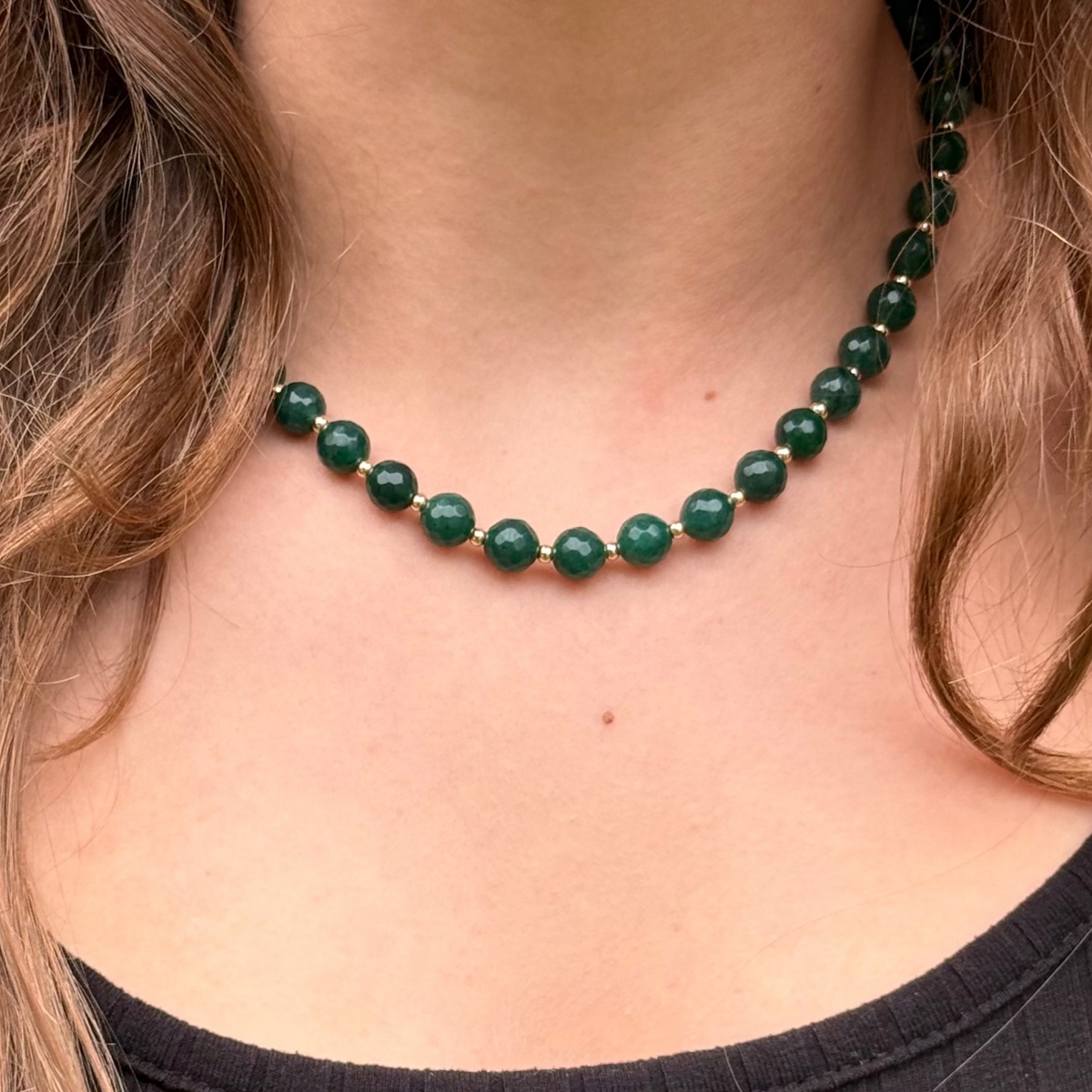 Large green emerald colored jade beads and tiny gold-beaded necklace on woman's neck