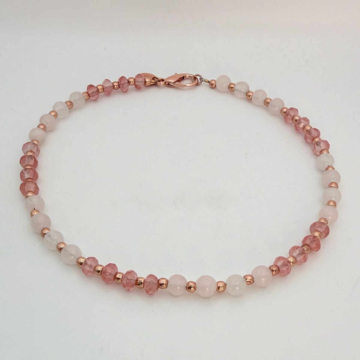 Studio photo of a flat laid Celia Quartz Necklace featuring pink faceted cherry quartz, smooth pale rose quartz beads, and rose gold plated accents.