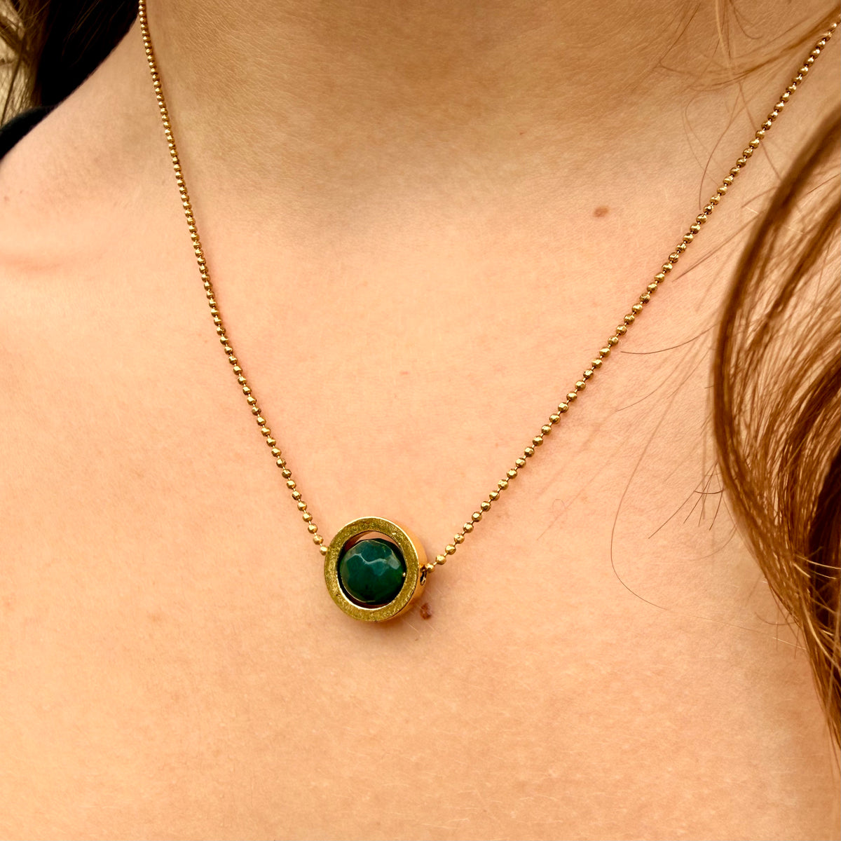Gold necklace with a green pendant on a person's neck