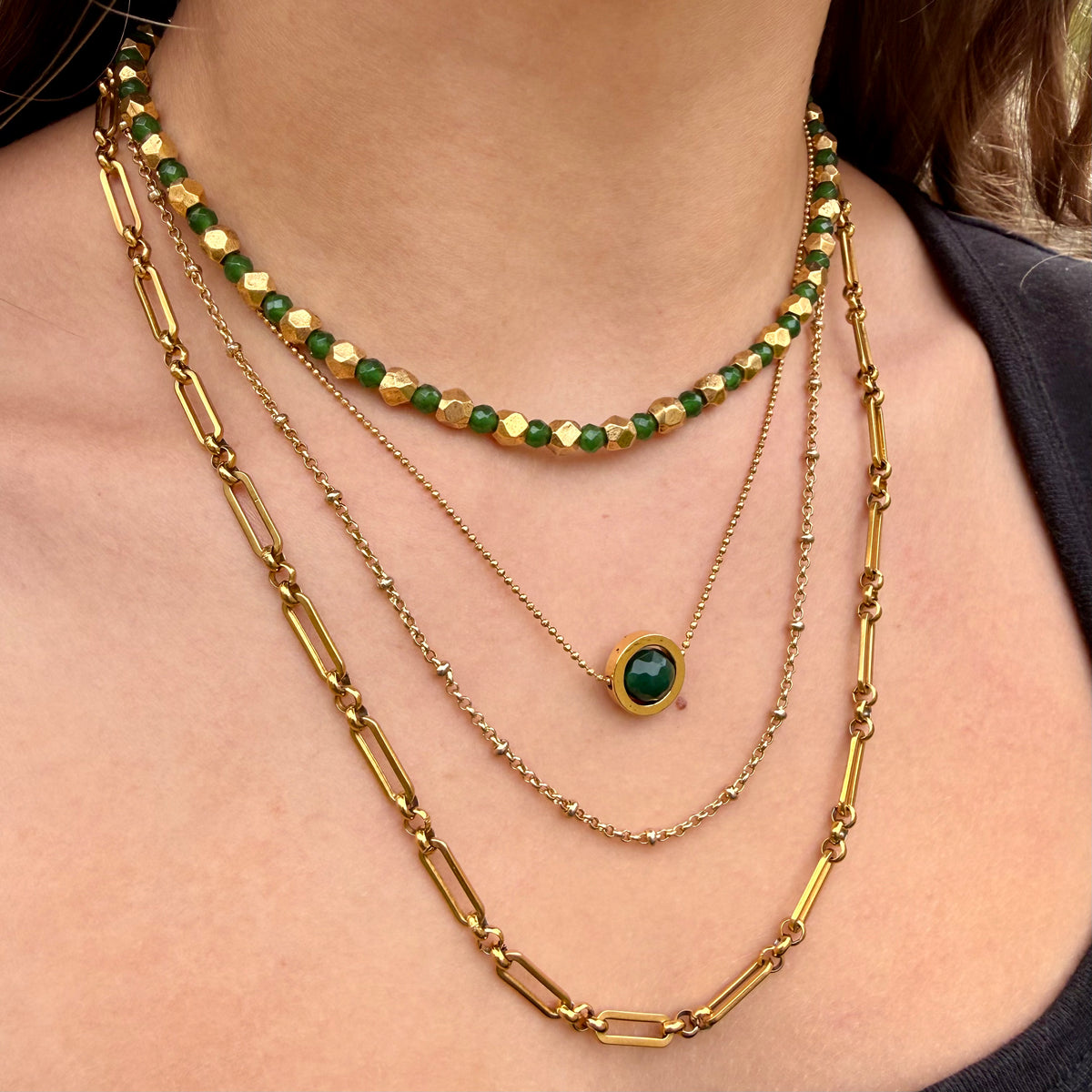 Stack of gold and green beaded necklaces on a person's neck
