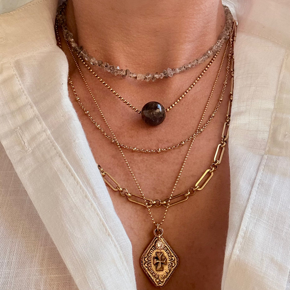 Layered gold necklaces with a central brown stone on a neutral background