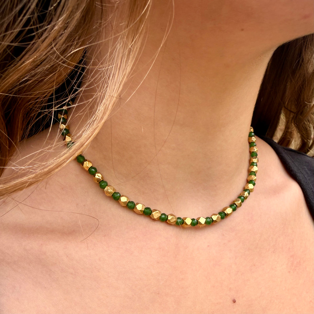 Close-up of a green and gold beaded necklace on a person's neck.