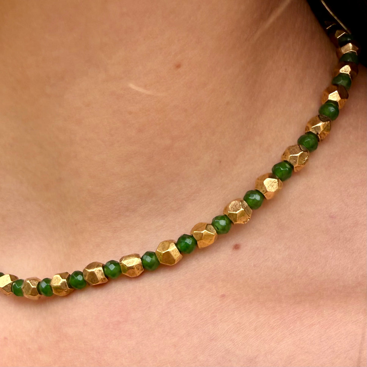 Necklace with green and gold beads on a person's neck