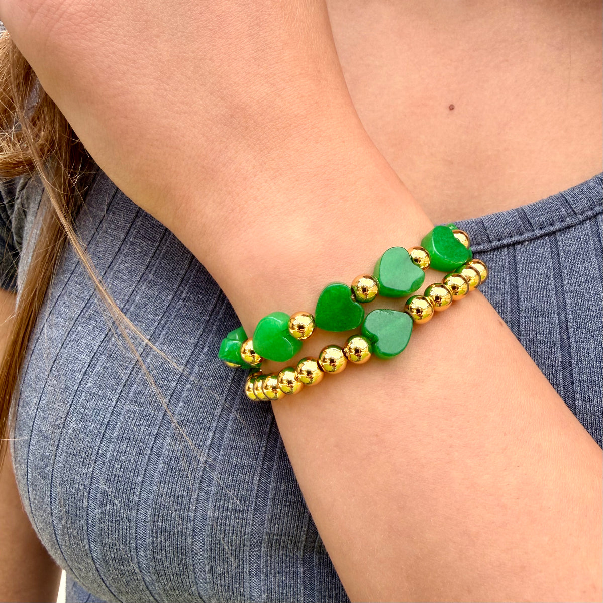 Green heart-shaped beaded bracelet with gold accents on a wrist against a denim background