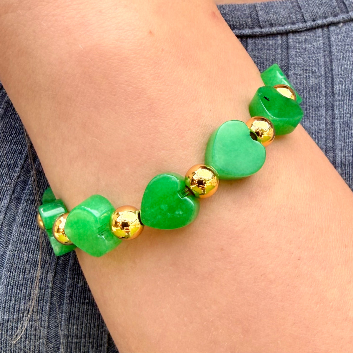Green heart-shaped beaded bracelet with gold accents on a wrist against a denim background
