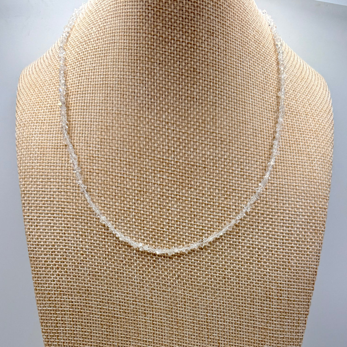 Necklace on a beige fabric-covered mannequin bust against a gray background