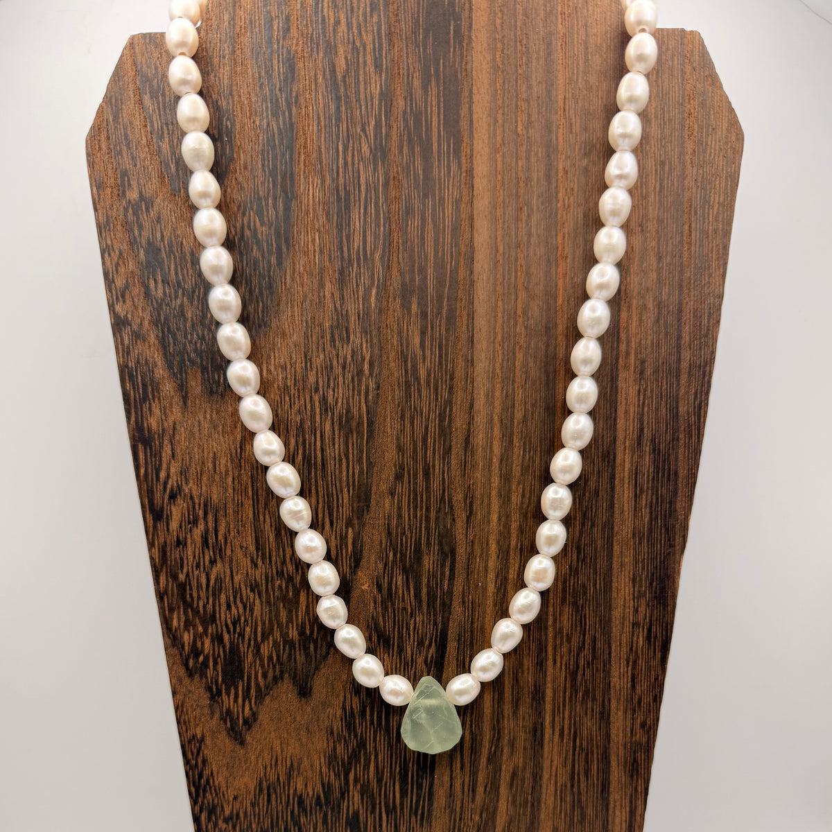 Pearl necklace with a green pendant on a wooden stand