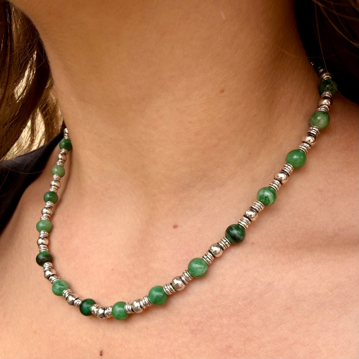 Necklace with green beads and silver accents on a person's neck