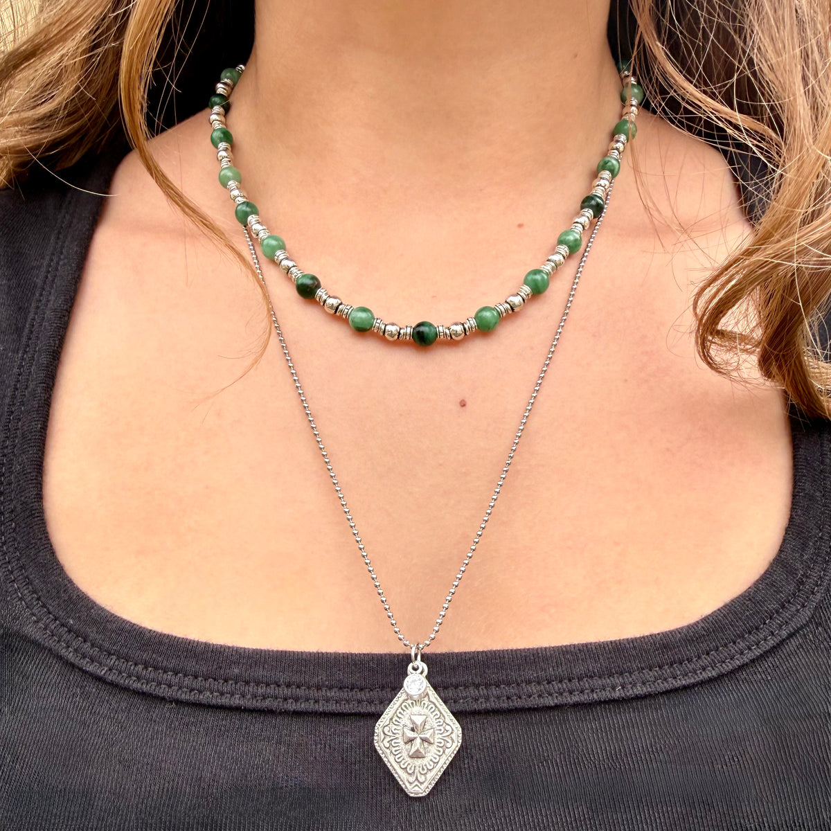 Close-up of a person wearing two necklaces with a dark top.