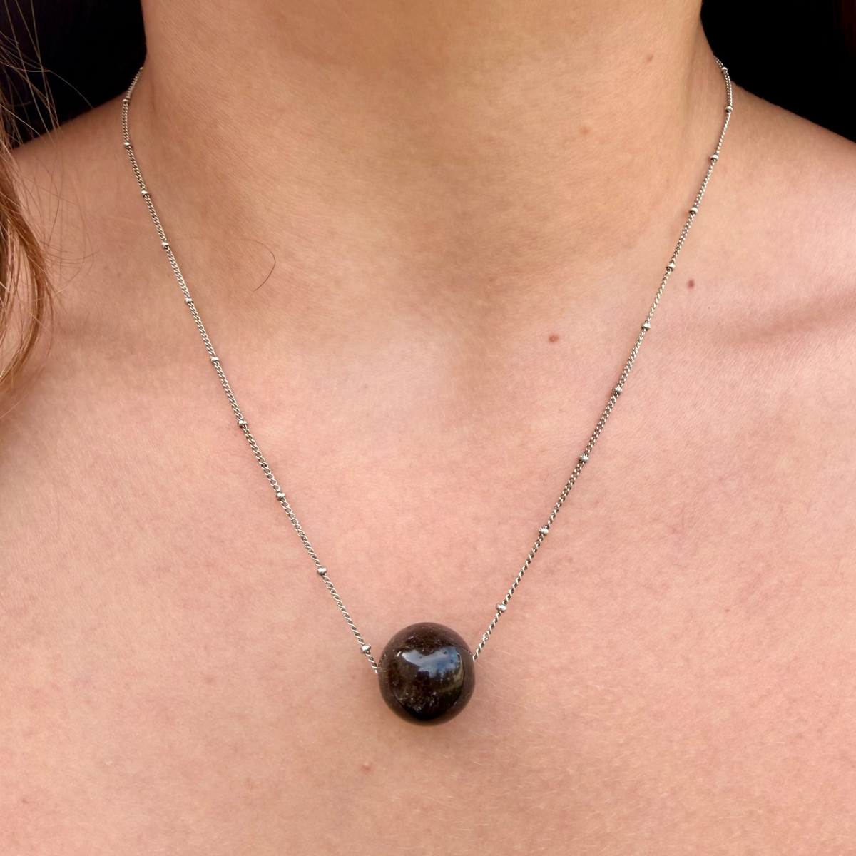 Necklace with a dark pendant on a person's neck against a neutral background