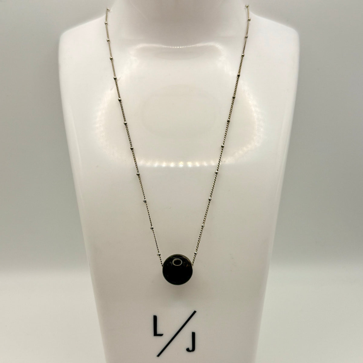 Necklace with a black pendant on a mannequin bust, branded 'LJ'.