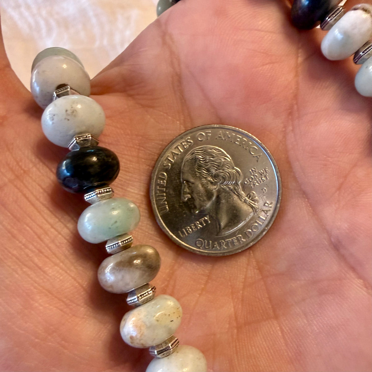A close-up of a beaded bracelet draped over a person's palm, shown next to a U.S.