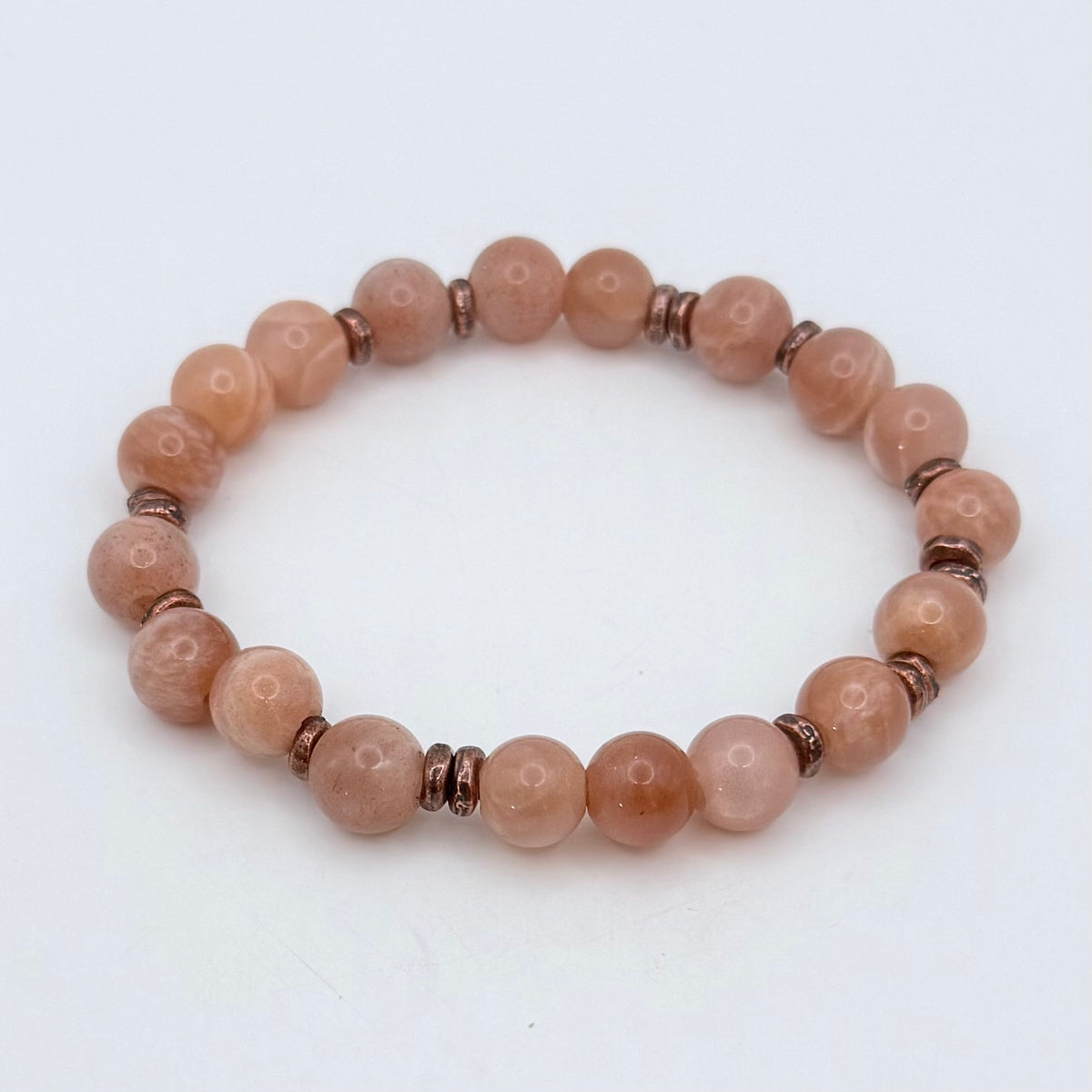 A beaded stretch bracelet made of smooth, round peach-pink stone beads separated by small metallic bronze spacer beads, shown on a plain white background.