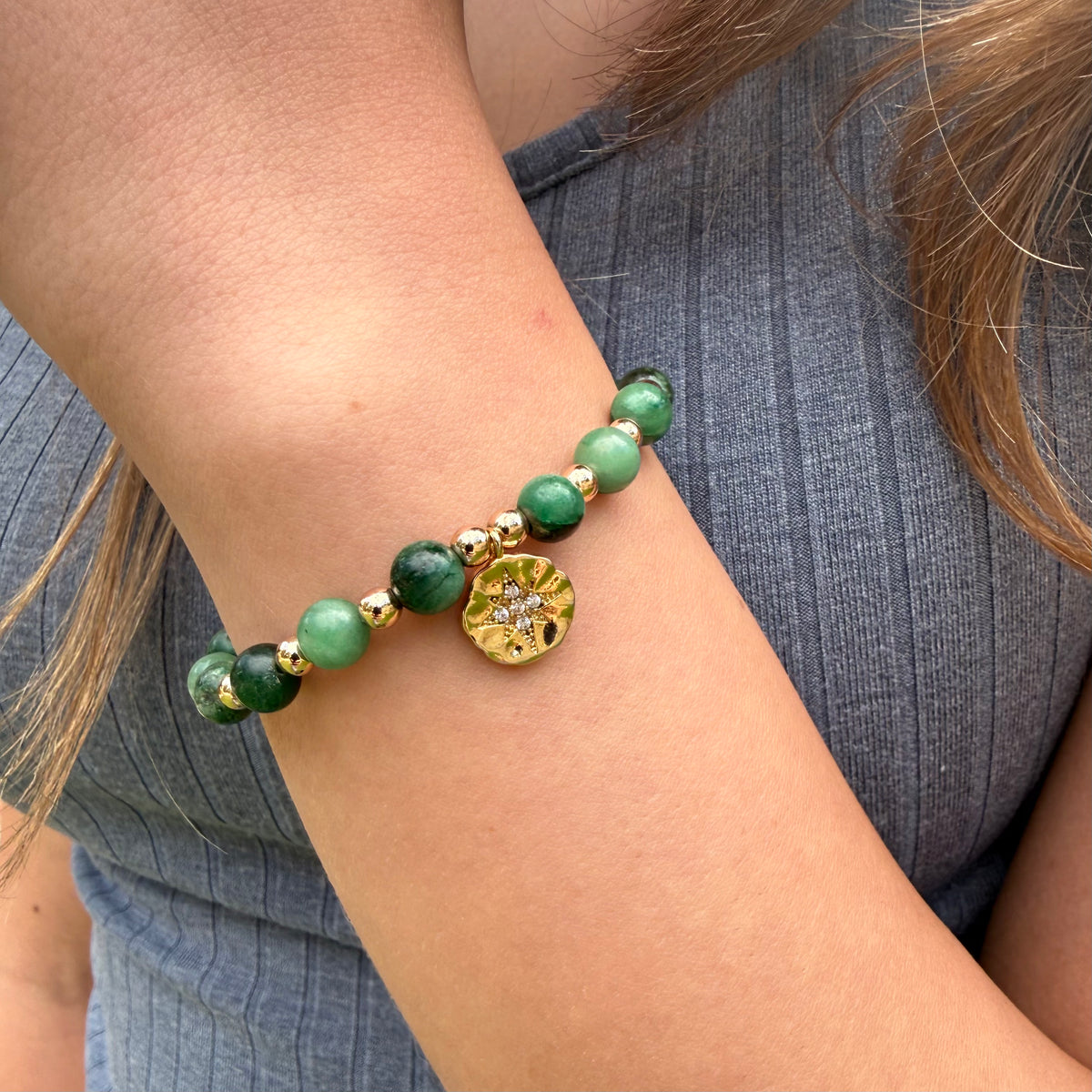 Green beaded bracelet with gold accents on a wrist against a blue shirt background