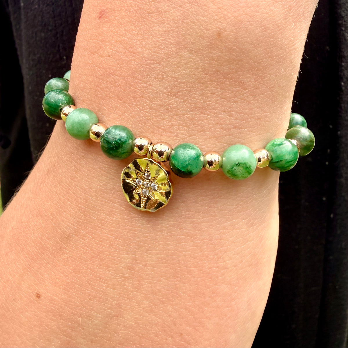 Green beaded bracelet with a gold charm on a wrist against a black background