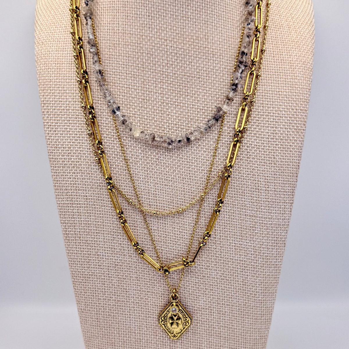 Gold necklace with a pendant on a mannequin bust against a plain background