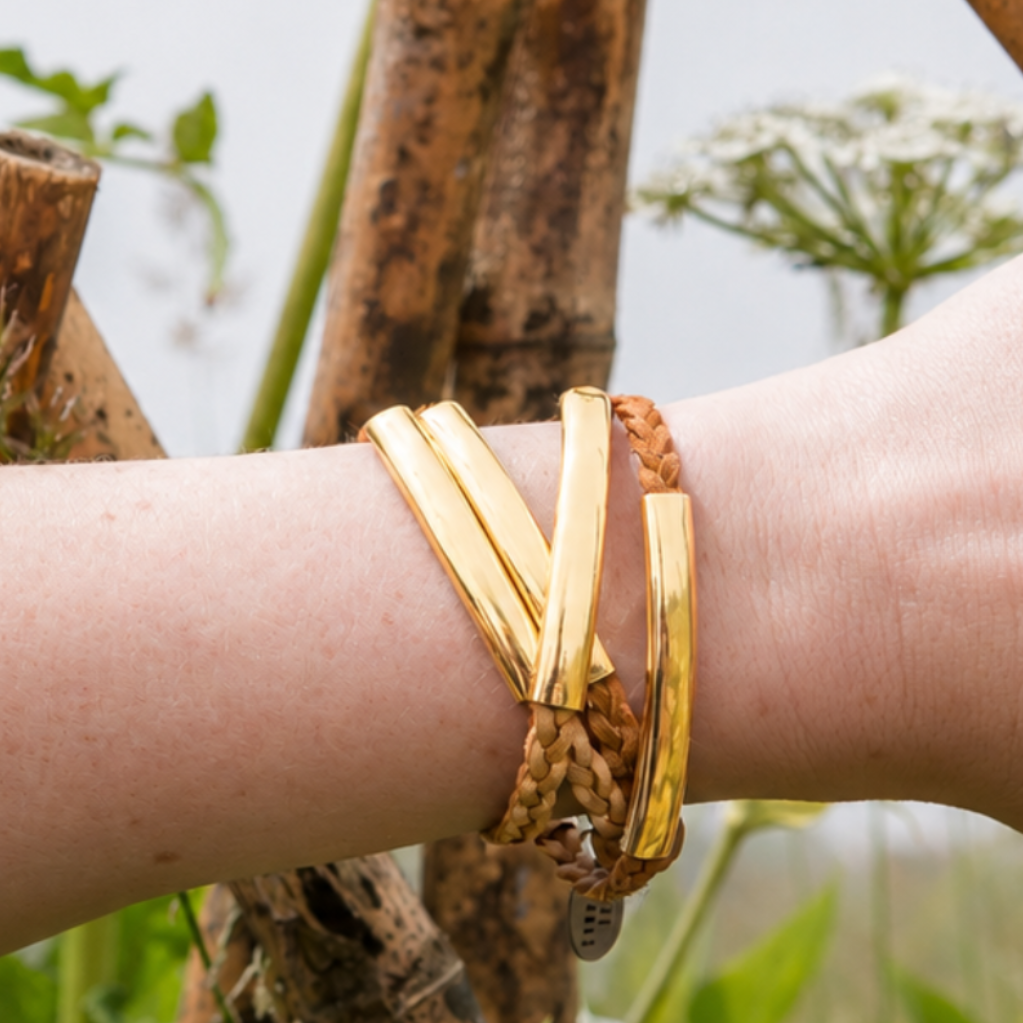Gold bracelets on a wrist with a natural background of plants