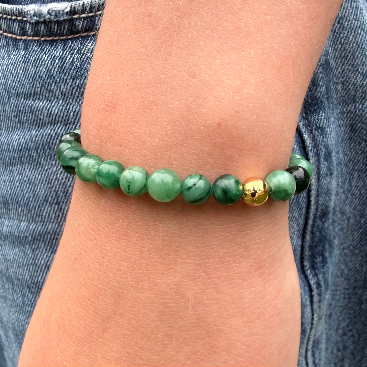 Green beaded bracelet on a wrist with denim background