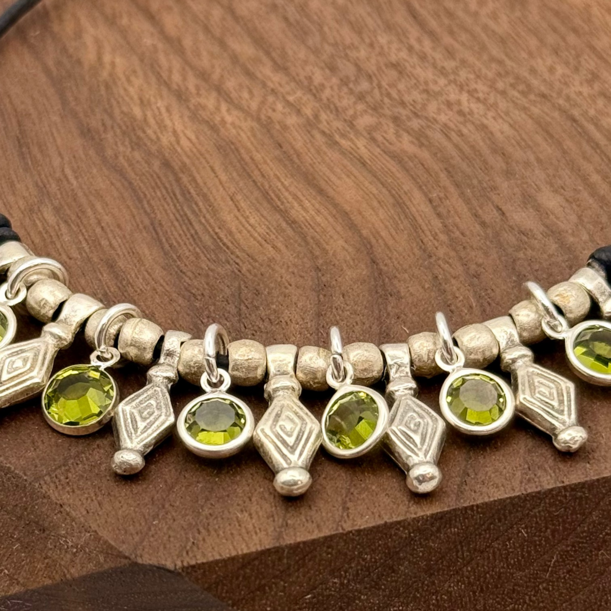 Bracelet with green gemstones and silver accents on a wooden stand