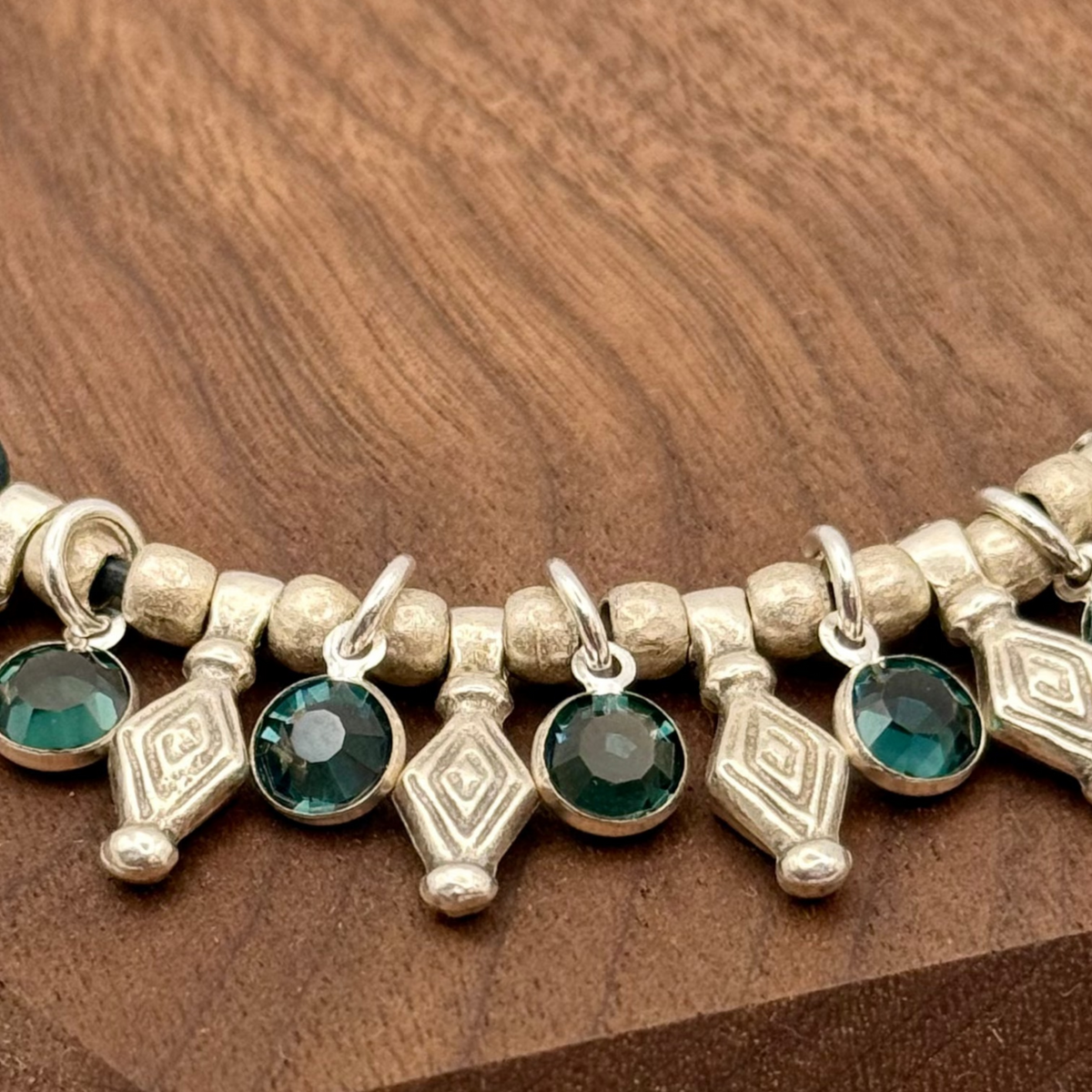 Bracelet with green gemstones and silver accents on a wooden stand