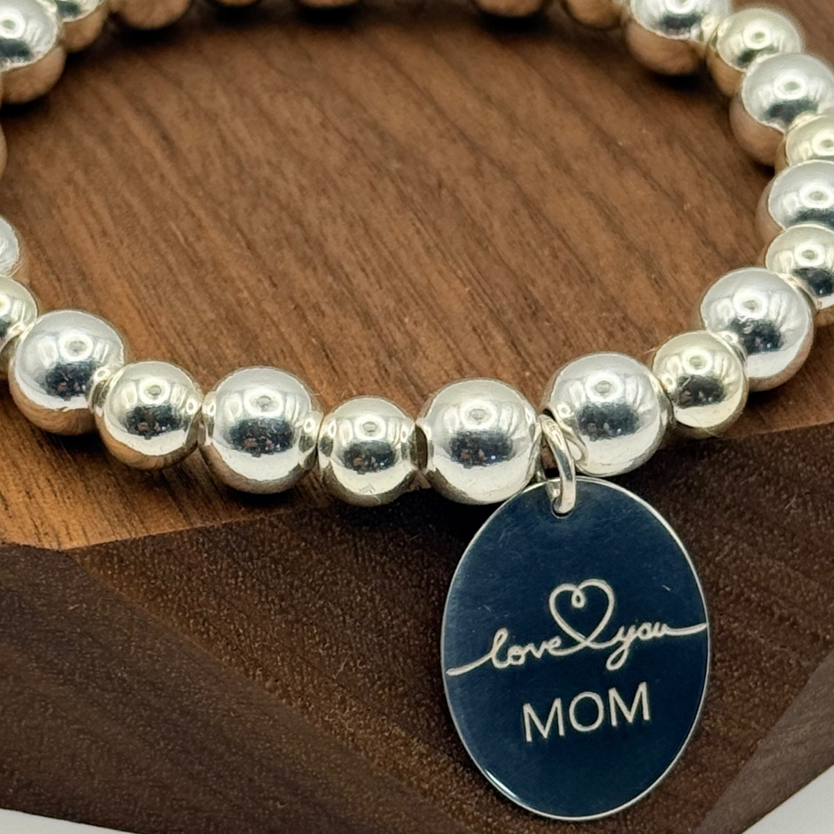 Silver beaded bracelet with a blue tag on a wooden surface